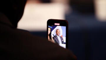 Photograph of Eric Adams smiling, seen through a smartphone recording him